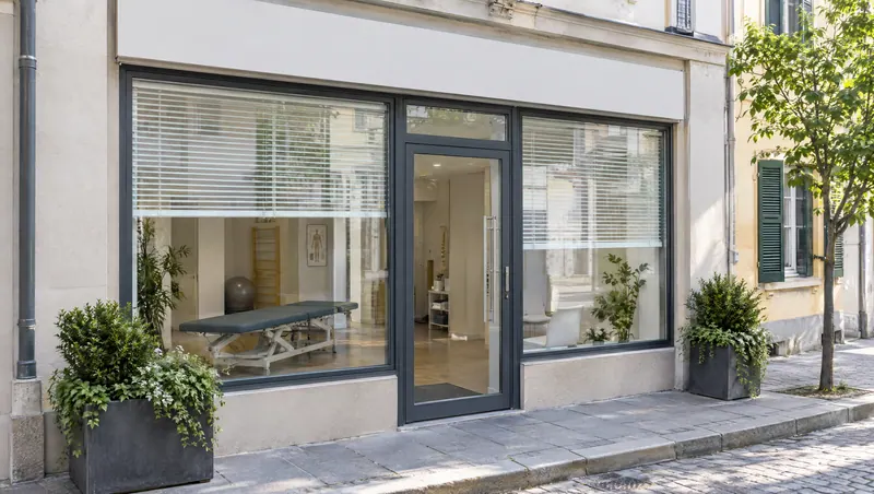 Street-level front of the clinic with large windows, a glass door and planters on a quiet street